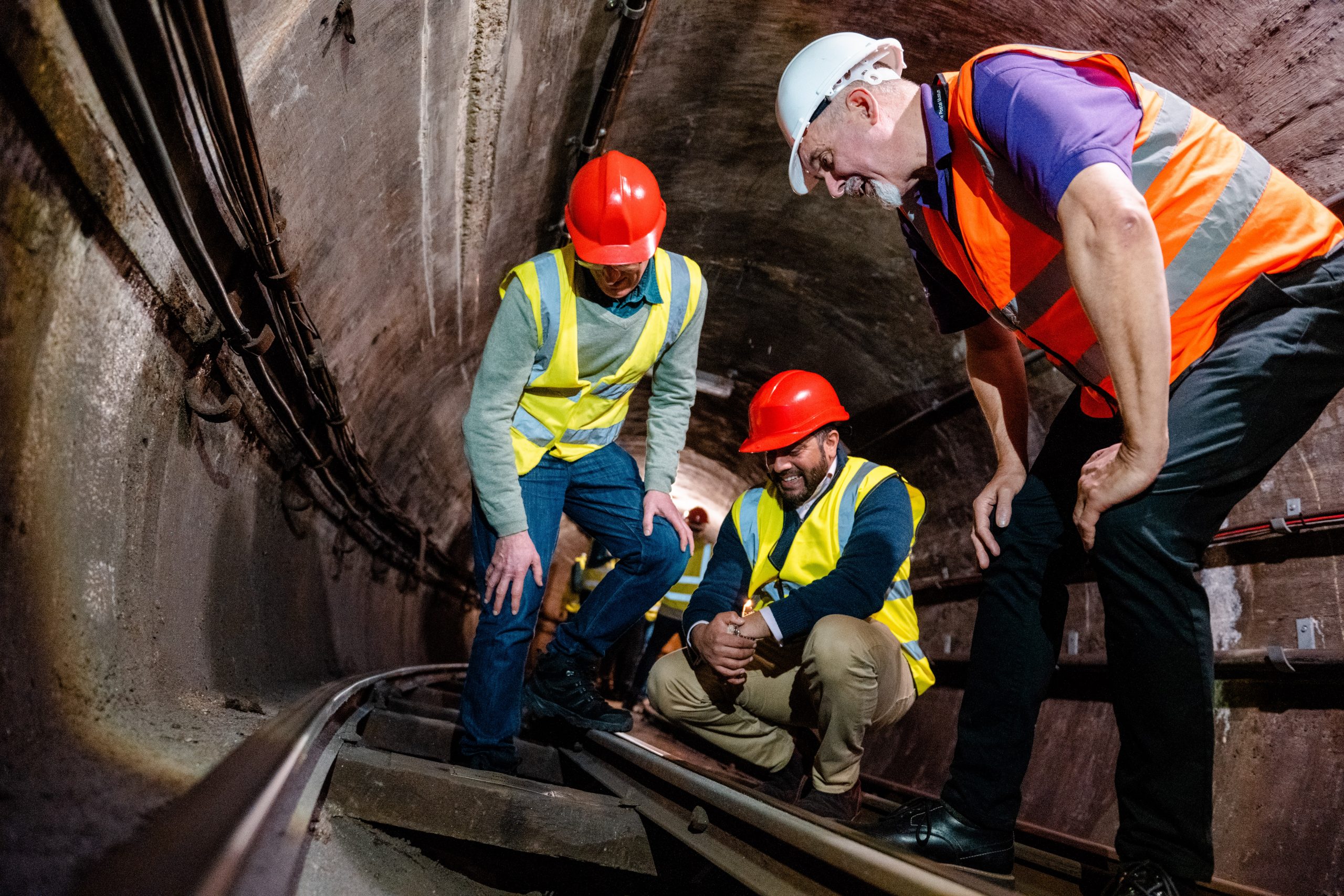 A group of people on high vis vests and hard hats look at one of the sleepers on the Rail Mail tracks