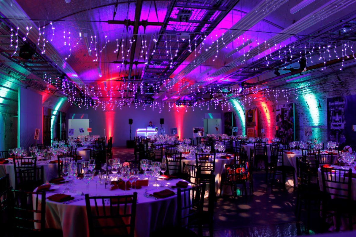 The Mail Rail venue hire space, set up with round tables, and purple and white string lights.