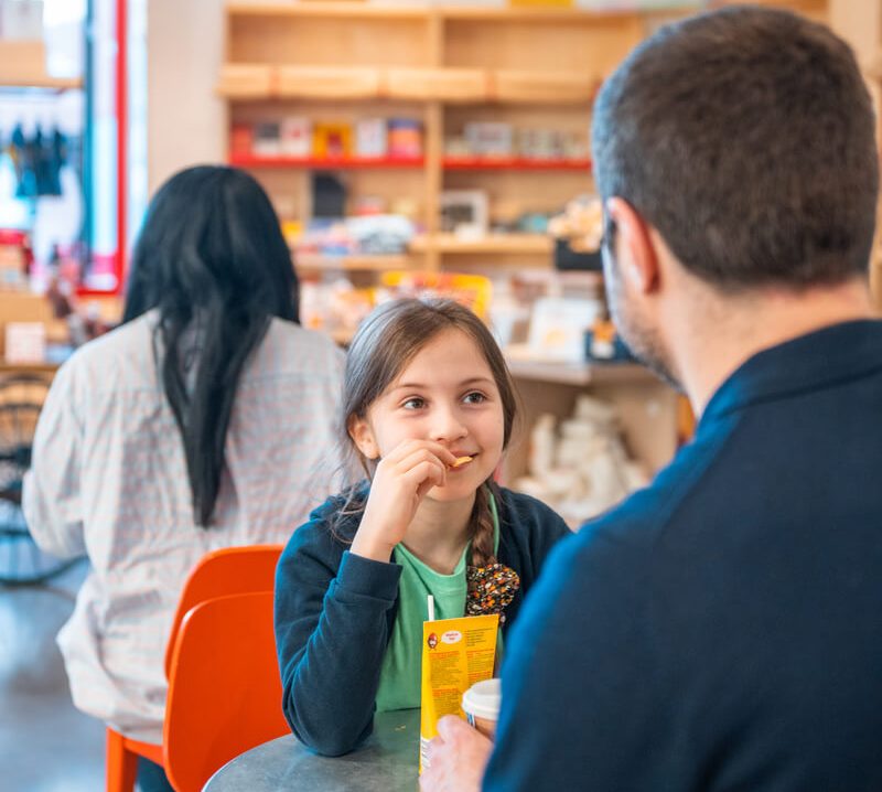 A girl and her dad talk while eating chips in the museum's cafe