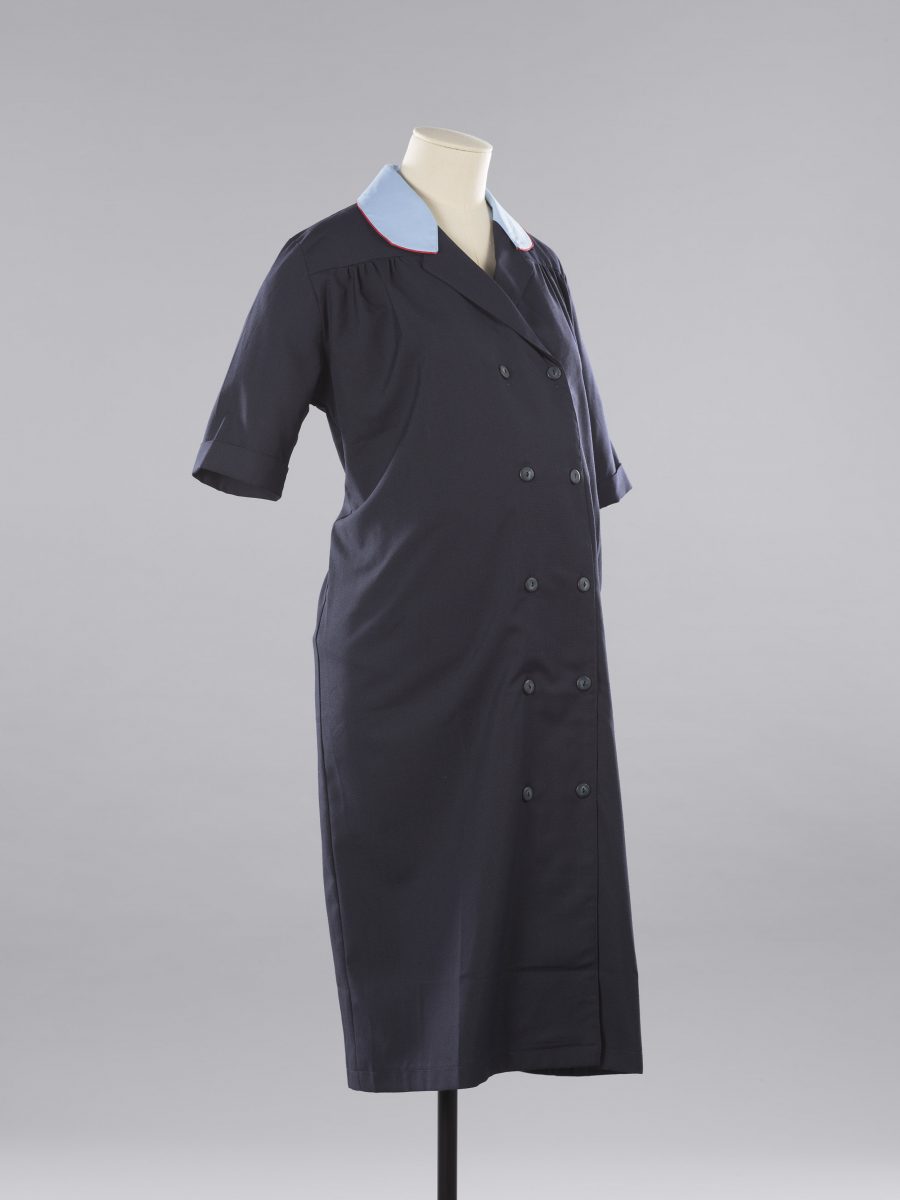 A dark blue maternity dress with light blue collar with red piping, and two rows of buttons going from the top to the bottom of it