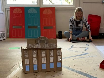 A carboard model of the museum's building, with big letters at the top of it reading Postal Museum.