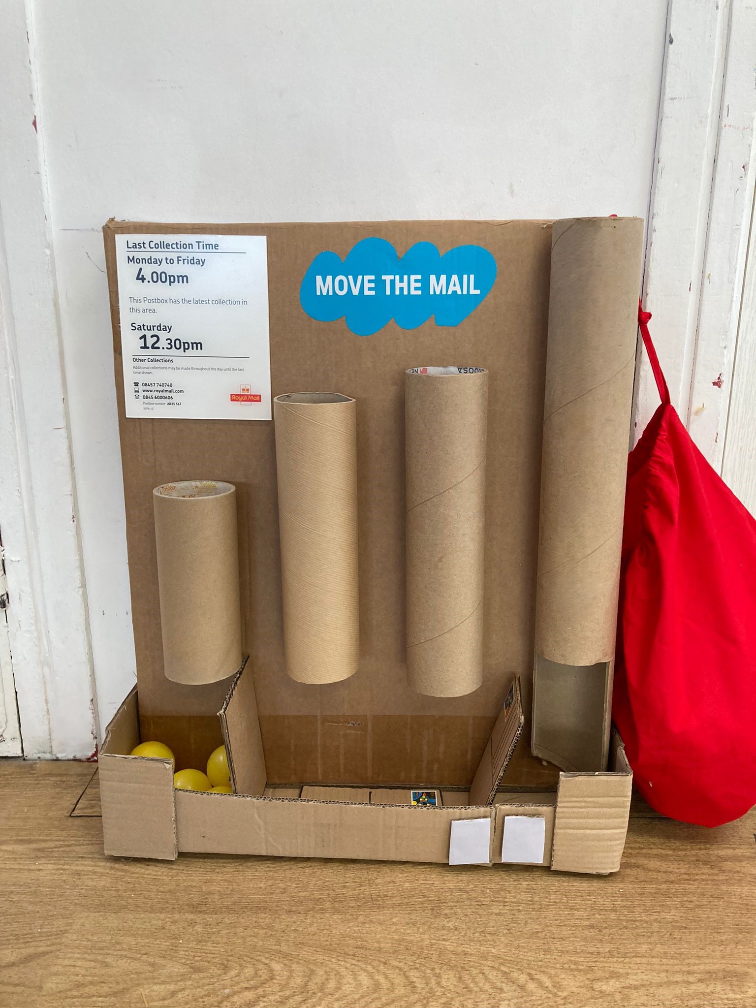 Carboard game with cylinders glued to a wall and holding boxes at the base, into which yellow balls are dropped.