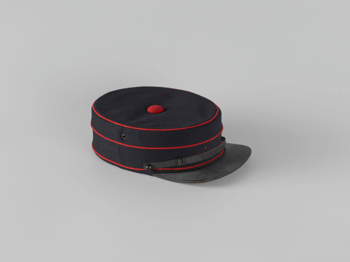 A blue pillbox cap with peak, red edges and red bottom at the top.