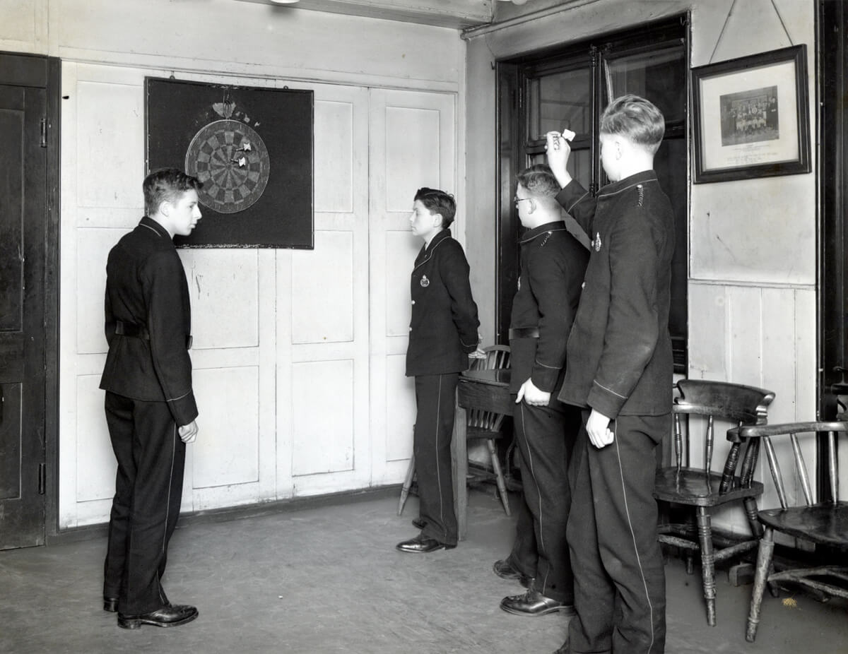 Four white boys in uniform play darts.