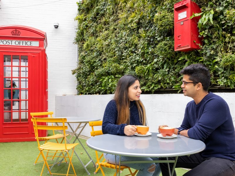 Two people drink coffee and chat while sitting at The Postal Museum cafe