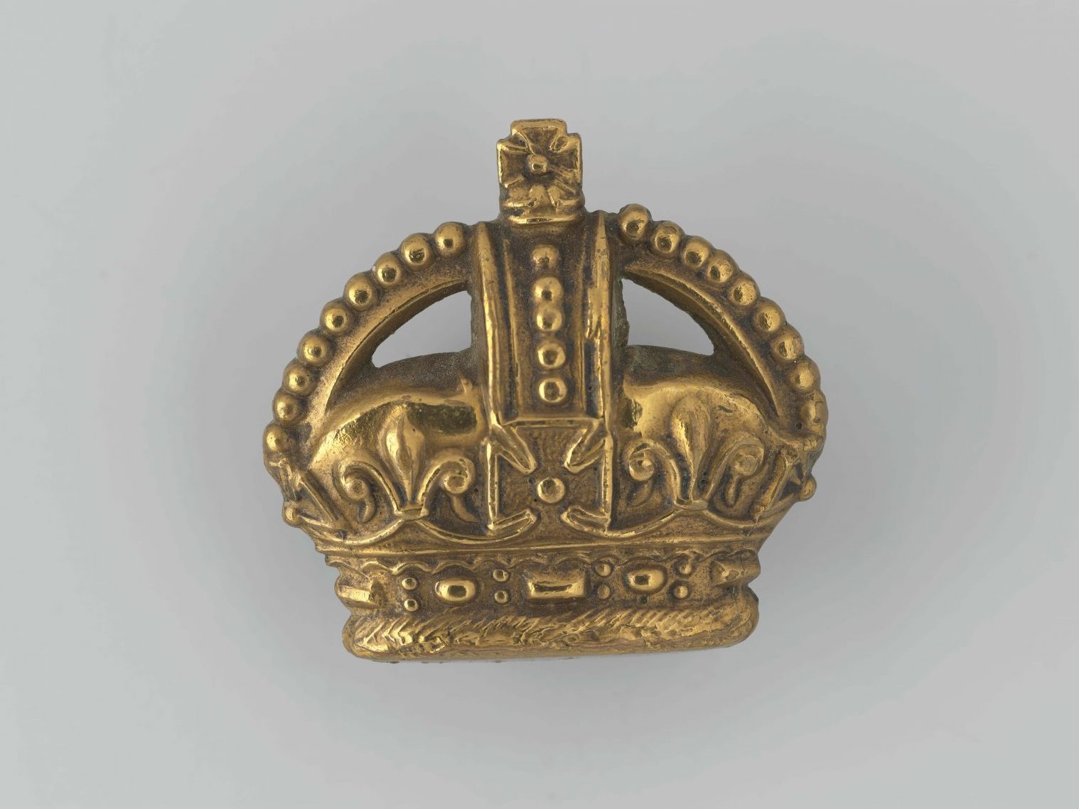 A crown with a top that curves to create a heart shape. The crown is decorated with fleur de lys, a lily flower with three petals, and a cross at the top and in the middle. Below the crown, the laurel leaves.