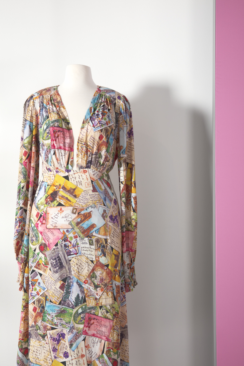 A cocktail dress decorated with a print made out of postcards and letters and displayed on a mannequin