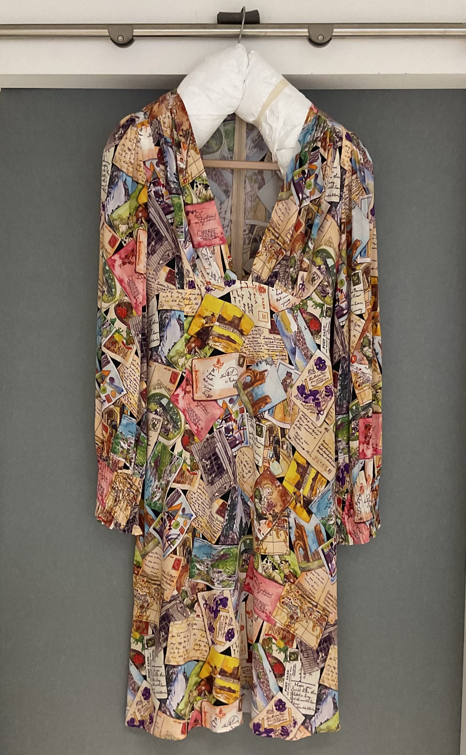 A cocktail dress decorated with a print made out of postcards and letters and hanged on a padded hanger