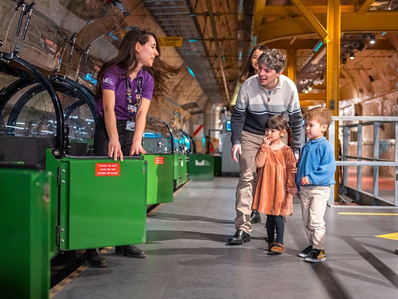 A family waiting to board the green miniature Mail Rail train at The Postal Museum.