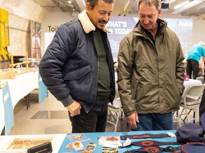 Two men look at a set of badges displayed on a table