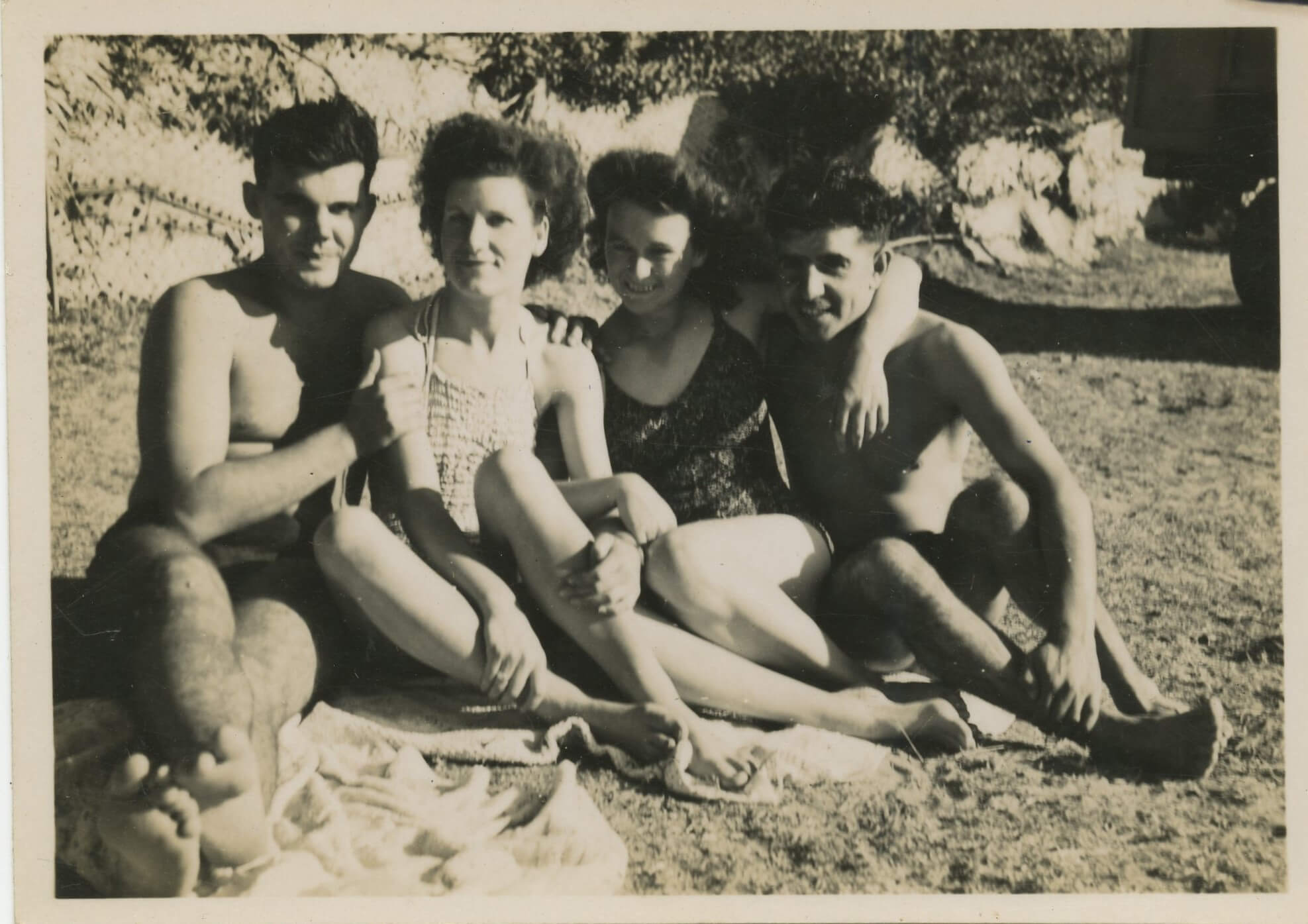 Two men and two women wearing swimming suits sat on the beach