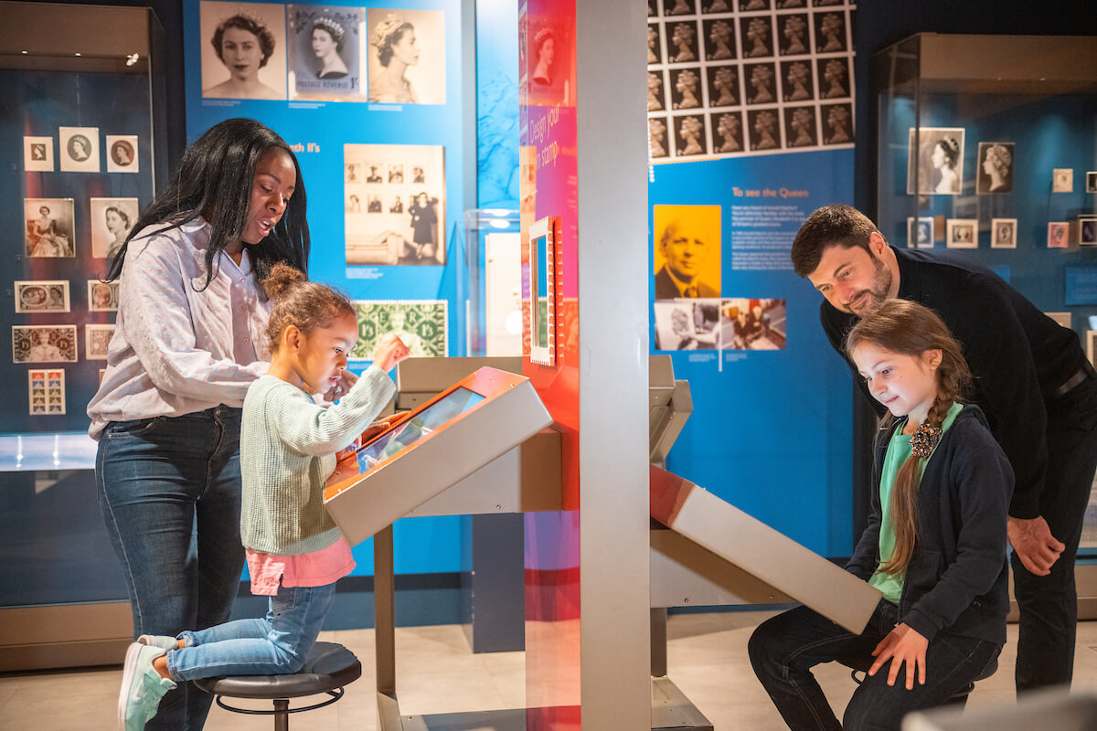 Parents and children looking at interactive screens in the museum gallery.