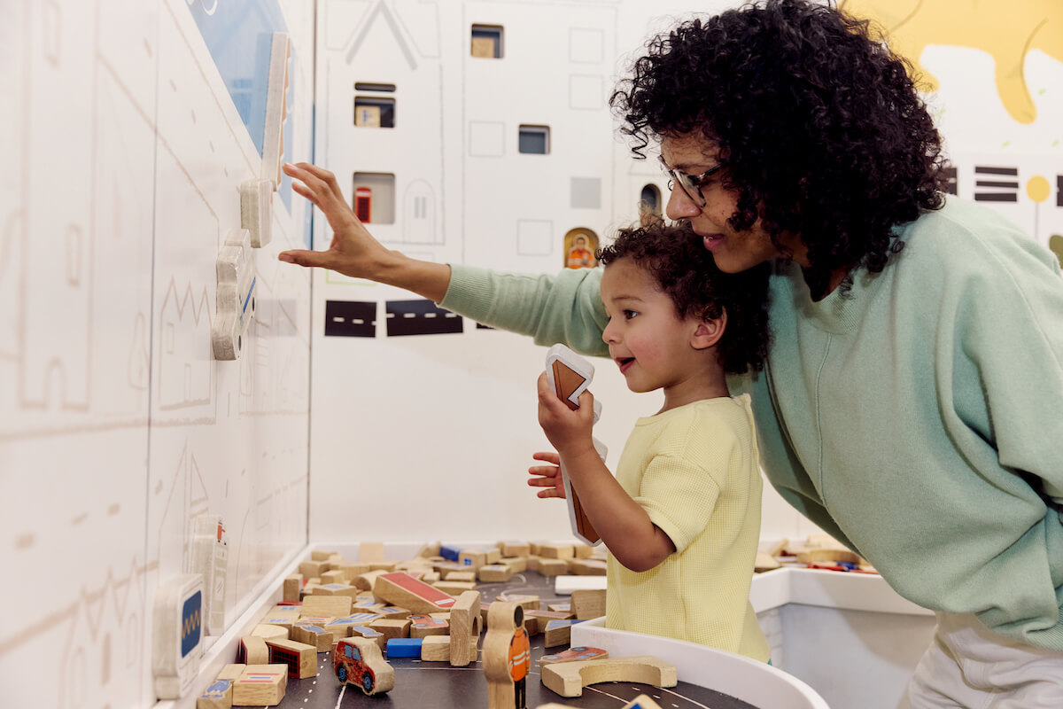 A parent and child playing with interactive blocks in a play space.