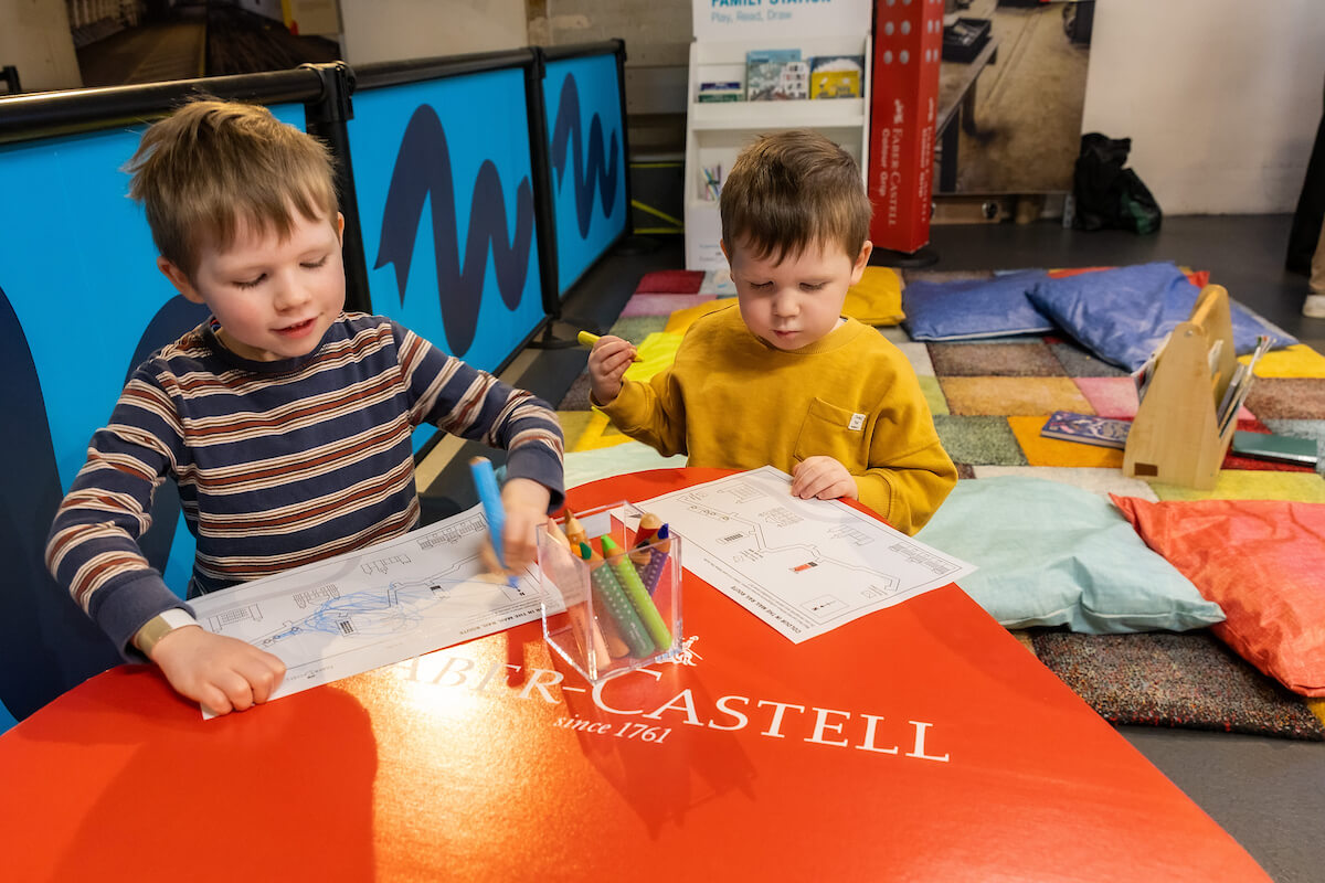 Two children playing with colouring activities at a craft table.