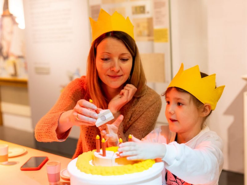 A parent and child playing with birthday-themed props in the exhibition.