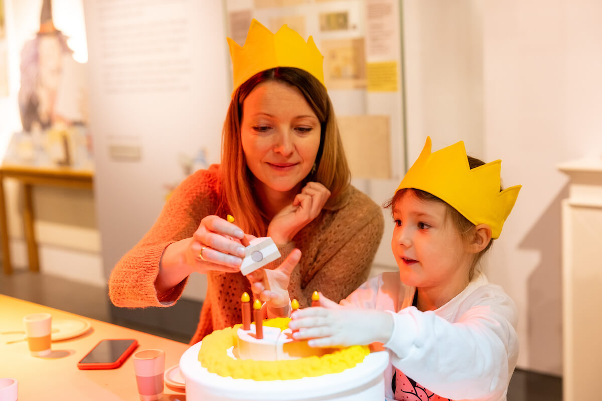 A parent and child playing with birthday-themed props in the exhibition.