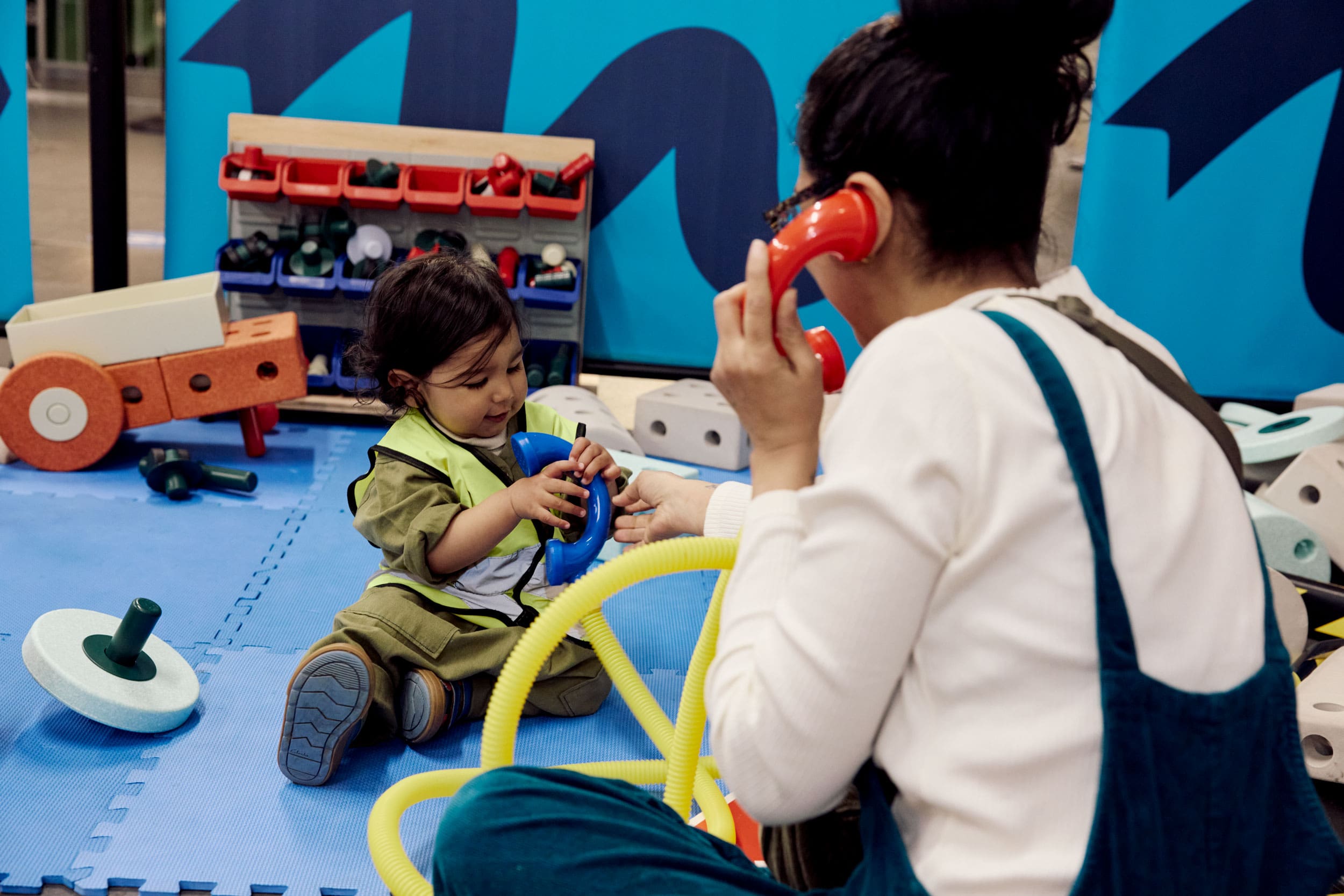 A mum 'answers' a call from her toddler on bright red toy phones with thick yellow tube as the cords.
