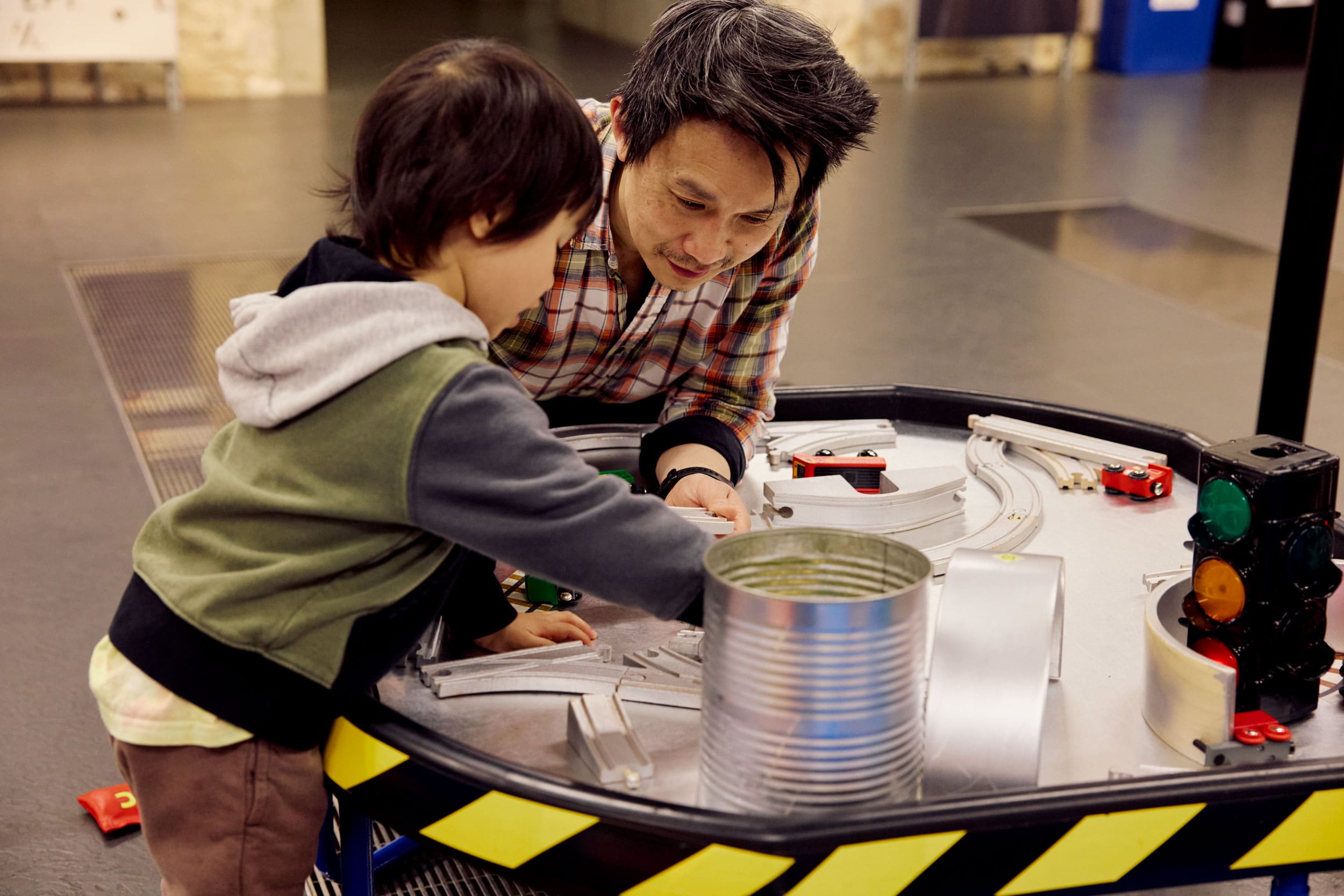 Father and son play with toy trains and train tracks. They look very invested in their play.