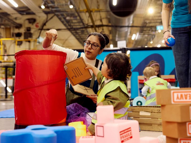 A young boy hands his mum a cardboard envelope to 'post' in a popup red Post Box.