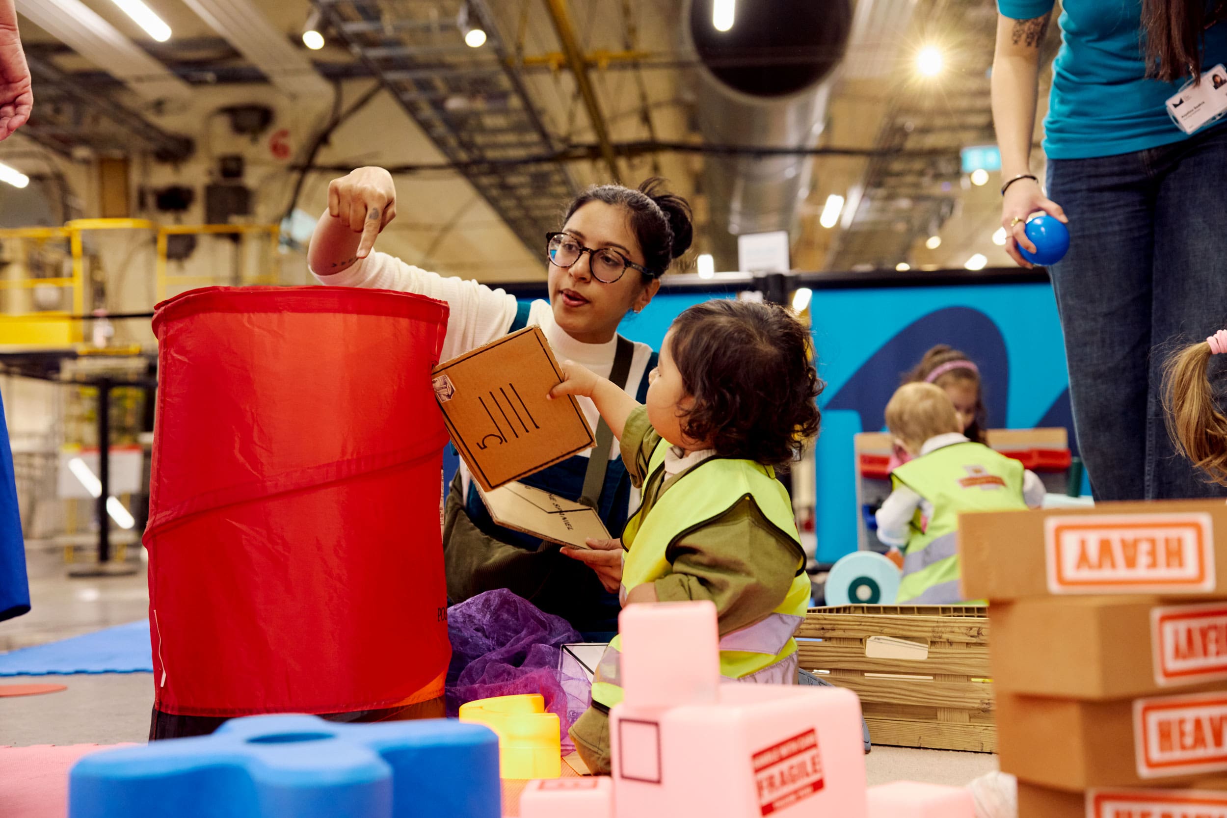 A young boy hands his mum a cardboard envelope to 'post' in a popup red Post Box.