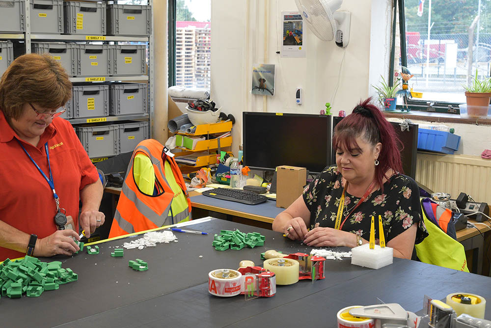 Two postal workers at a worktable, working with crafting and modelling materials.