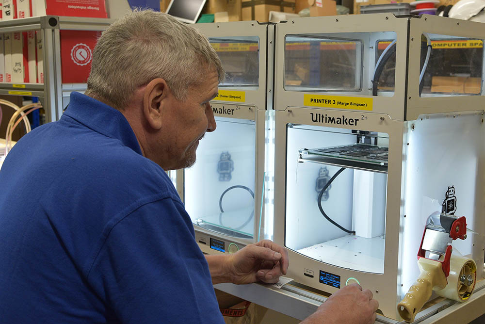 A man in blue uniform works at a 3D printing machine.