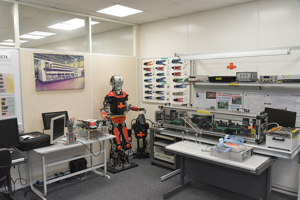 A room with tools, computers and a robot standing in the corner.