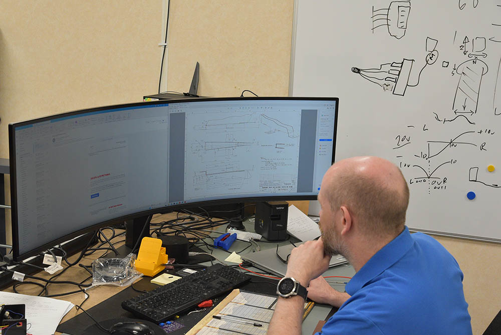 A man in blue uniform works at a computer desk.