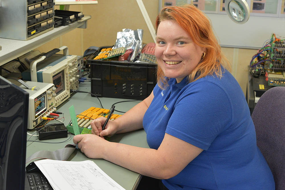 A woman in blue uniform working with tools at a desk.