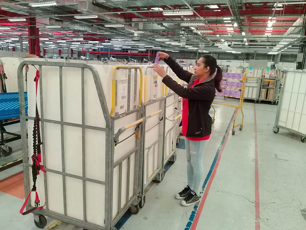 A woman in postal uniform with a mail trolley.