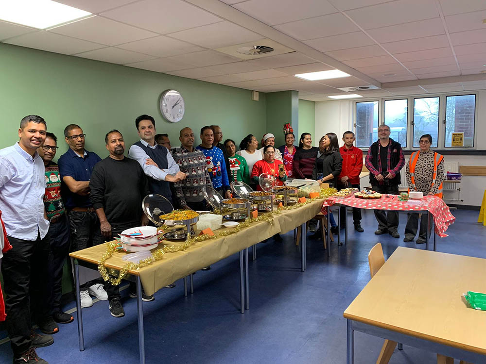 A large group of postal workers at a long table at a party, with Christmas decorations and festive jumpers.