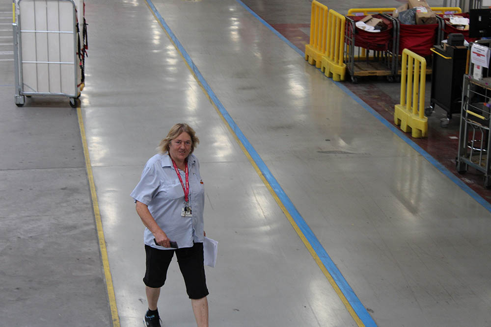 A woman walking through the Royal Mail site in a postal worker uniform.