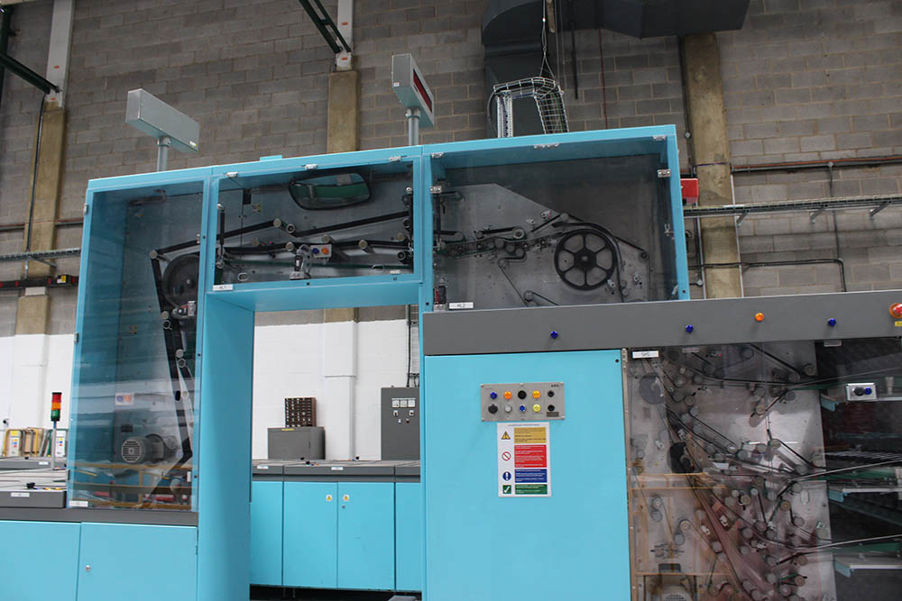 The side of a large blue machine with a clear panel, showing moving parts inside the machine.