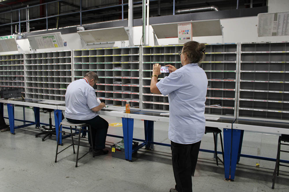 Postal worker seated at a desk next to sorting equipment.