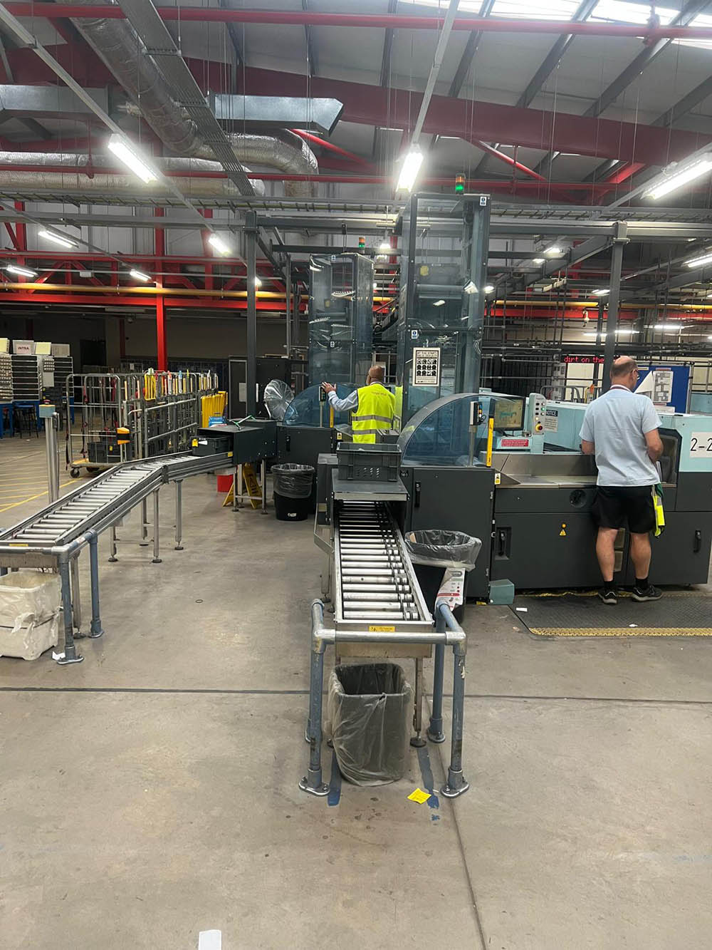 Postal workers working on a machine and conveyor belt in the mail centre.