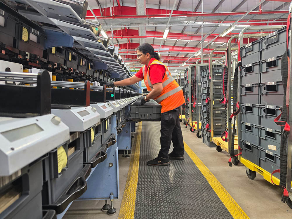 A woman in red postal uniform working with sorting equipment.