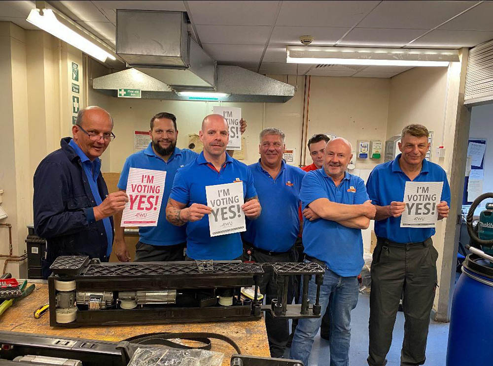 A group of workers in blue postal uniform, holding up signs saying 'I'm voting yes!'