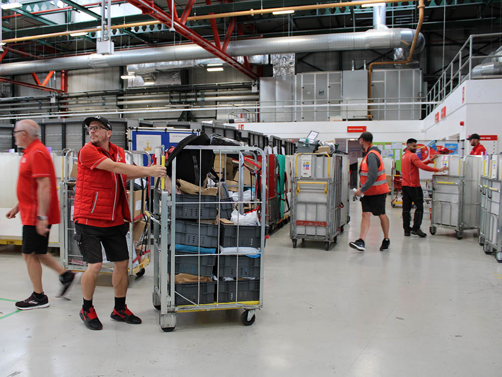 Uniformed postal workers with trolleys at the delivery office.
