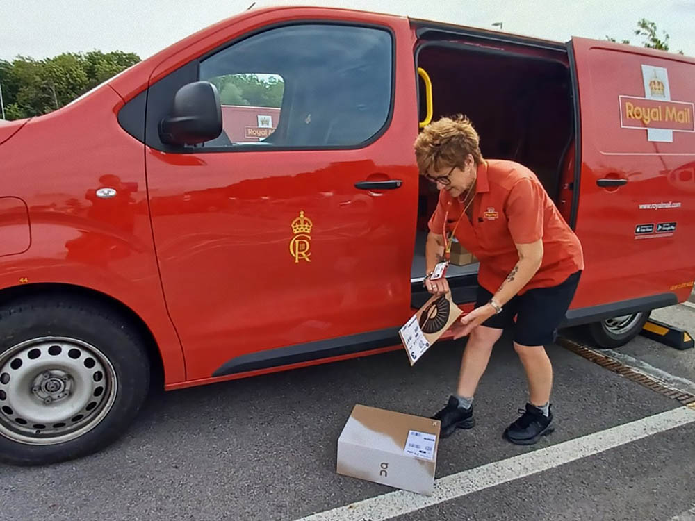 Uniformed driver taking mail out of a red postal van.