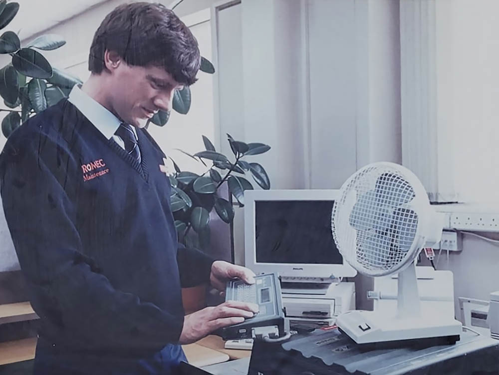 An engineer in an old blue postal uniform, working at a computer.