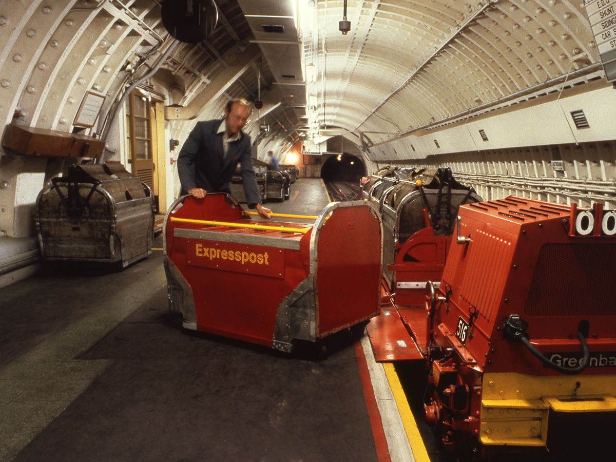 A man pushing a Mail Rail York - a red and yellow trolley with the words 'Express Post' stamped on the side.