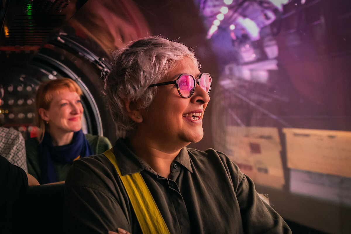 Women riding a miniature train, looking out at a projected display in the tunnels.